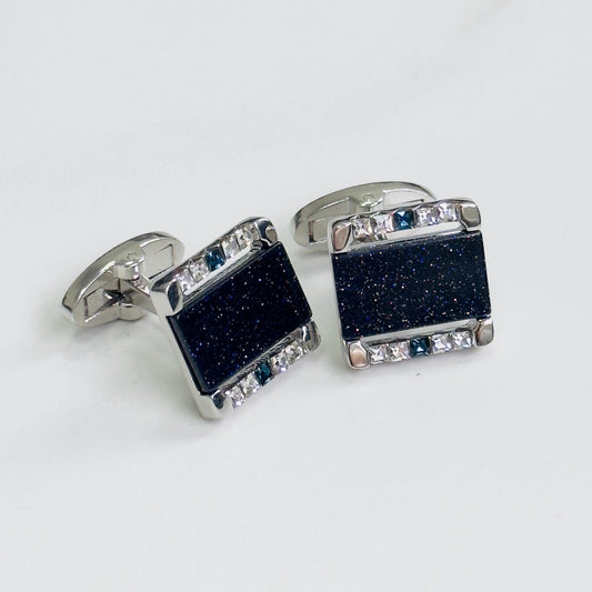Square cufflinks with blue textured centers and clear gem borders on a white background.