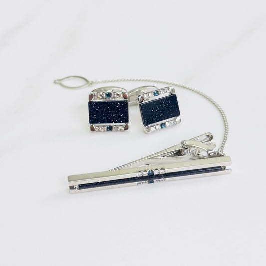 Cufflinks and tie clip set with blue stones and clear gem accents on a white surface