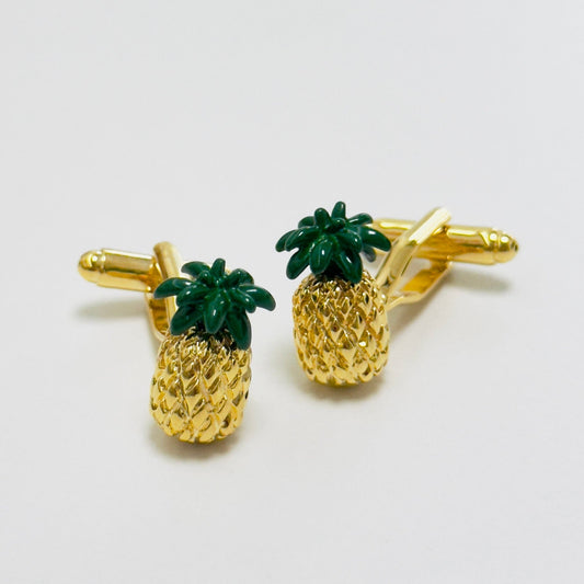 A pair of pineapple-shaped cufflinks with gold-tone bodies and green leaves, featuring detailed texturing.